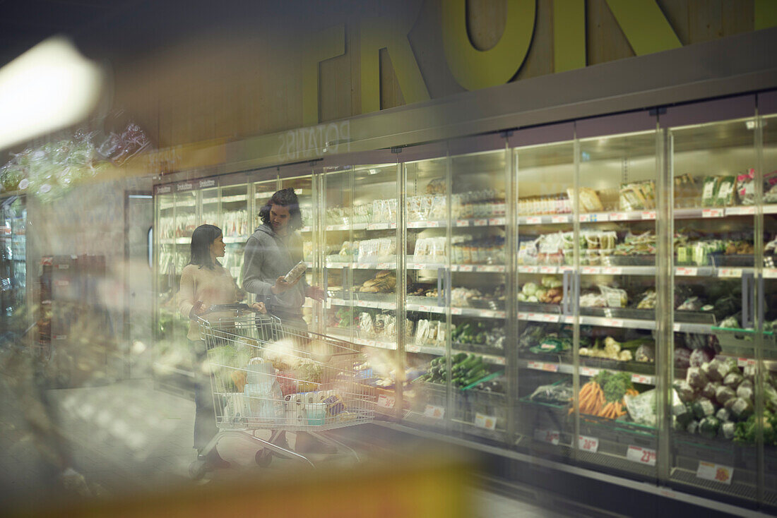 Couple in supermarket choosing vegetables from fridges