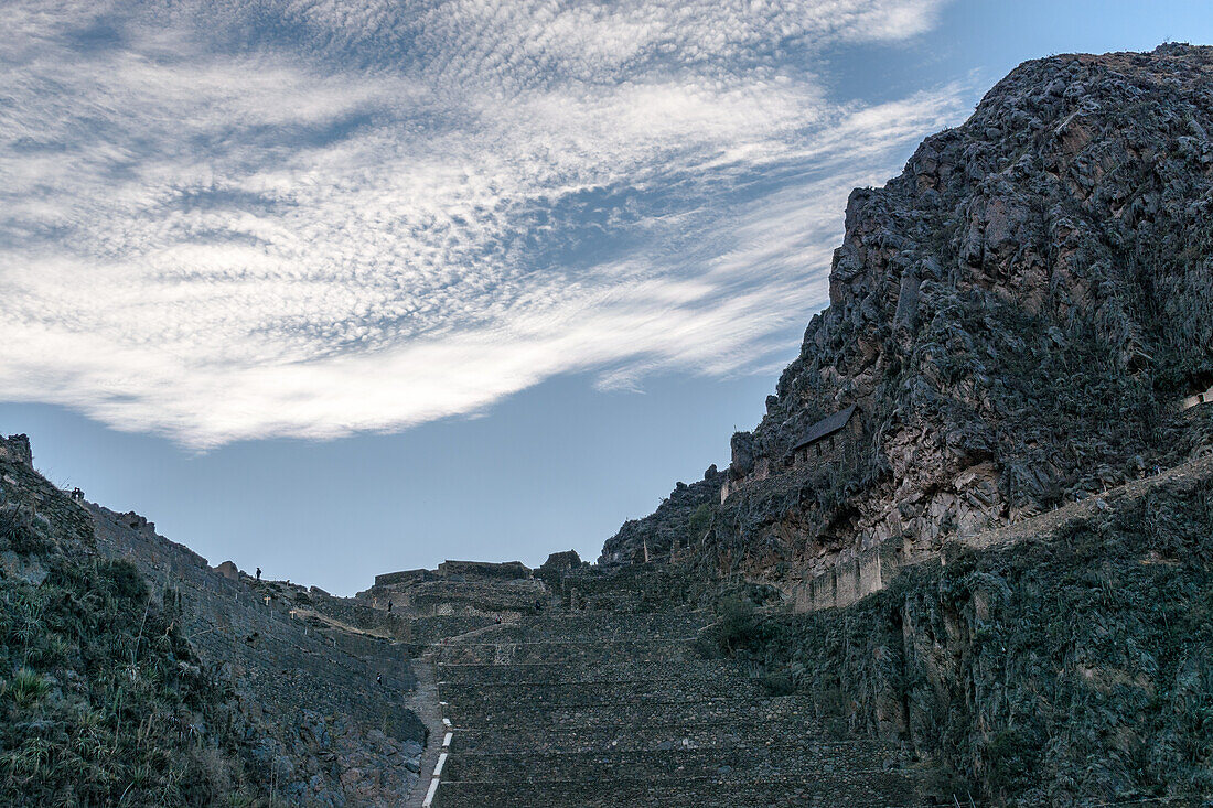 Ollantaytambo, Steinstufen und Terrassen an einer steilen Felswand in den Bergen, kleine Häuser und Menschen auf dem Weg.