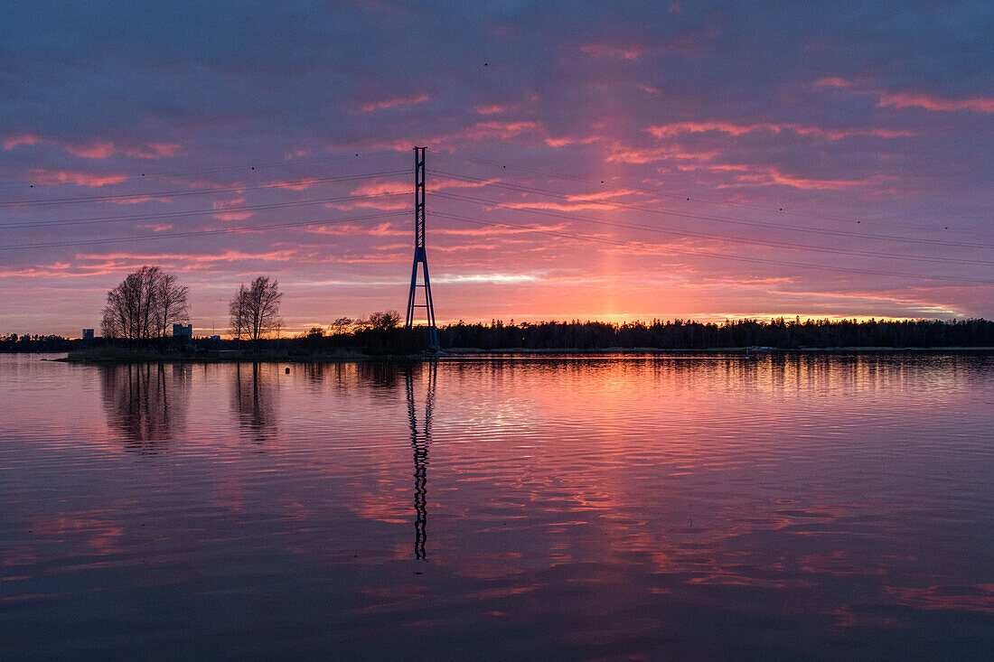 A view of a tall mast and buildings on the coastline of islands  near Helsinki, at sunset.