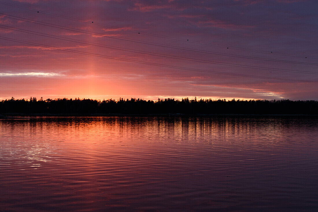 Die Küstenlinie der Inseln bei Helsinki, bei Sonnenuntergang, ein rotes Leuchten am Himmel.