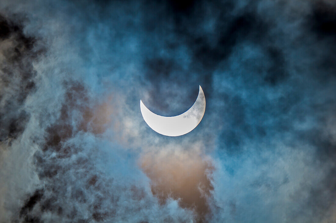 Die partielle Sonnenfinsternis, 23. Oktober 2014, von Jasper, Alberta, aus gesehen, in diesem Fall durch eine dünne Wolke hindurch aufgenommen, was aber ein interessanteres Foto ergibt als bei klarem Himmel. Diese Aufnahme wurde durch einen Mylar-Filter auf der Vorderseite eines 66-mm-Apo-Refraktors mit der Canon 60Da bei einer Belichtungszeit von 1/25 s und ISO 100 gemacht. Die Farben sind natürlich, wobei der Mylar-Filter ein neutrales Weißlichtbild liefert. Da die Sonne durch die Wolken stark verdunkelt war, ermöglichte die längere Belichtung das Aufnehmen von Licht und Farben in den umlieg