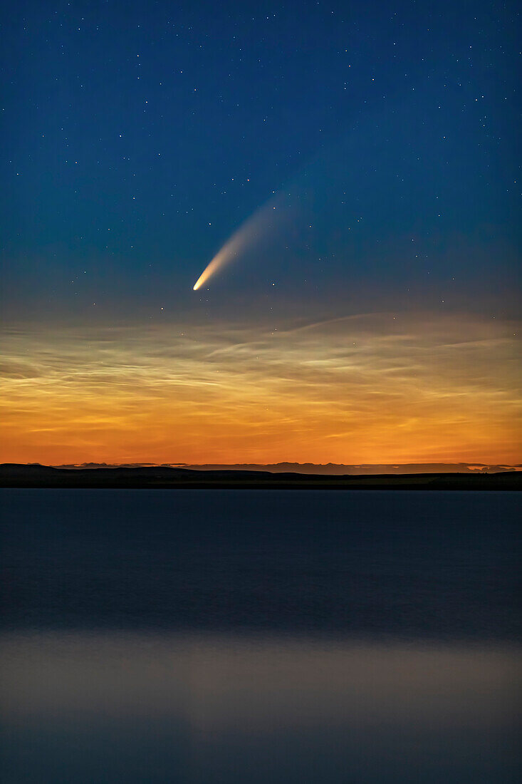 Dies ist der Komet NEOWISE (C/2020 F3) über dem Deadhorse Lake in der Nähe von Hussar in Süd-Alberta, aufgenommen kurz nach Mitternacht am 10. und 11. Juli 2020 während seiner abendlichen Erscheinung. Der Komet leuchtet knapp über tief hängenden, nachtleuchtenden Wolken. Der leichte Wind hat das Wasser so aufgewühlt, dass die von mir angestrebte saubere Reflexion nicht zustande kam.