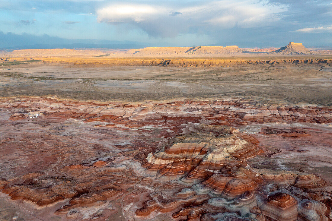 Luftaufnahme des ersten Lichtes auf Factory Butte mit den farbenprächtigen Bentonite Hills im Vordergrund, in der Nähe von Hanksville, Utah.