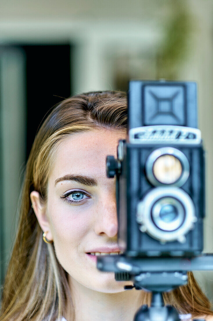 Porträt einer jungen schönen kaukasischen Frau in den 20ern mit blauen Augen, die mit einer alten Vintage-Kamera auf einem Stativ im Freien fotografiert. Lifestyle-Konzept.
