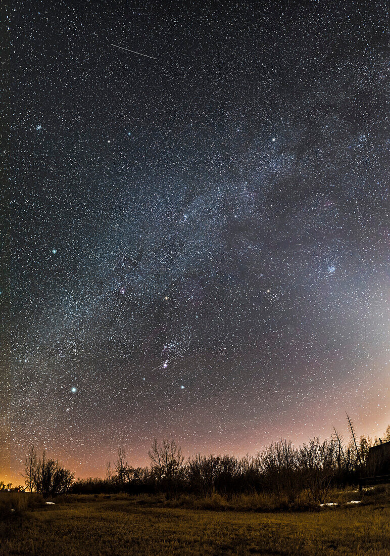 A horizon-to-zenith panorama of the winter consellations on a March evening as they set into the southwest. Orion is at bottom centre, with his Belt pointing down to Canis Major and up to Taurus. Gemini and Auriga are at top, in this case near the zenith overhead. The bright star clusters, M44, the Beehive, (at left) and M45, the Pleiades, (at right) flank the Milky Way. M45 is embedded in the Zodiacal Light. The star clusters M35 in Gemini and M41 in Canis Major are also visible as diffuse spots, as are several other star clusters. A couple of satellite trails are visible.