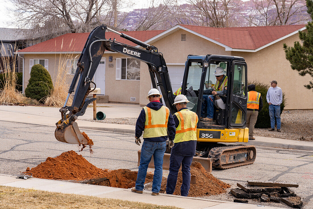 A utility worker uses a track hoe to excavate a hole in the street to repair a utility line in a neighborhood.