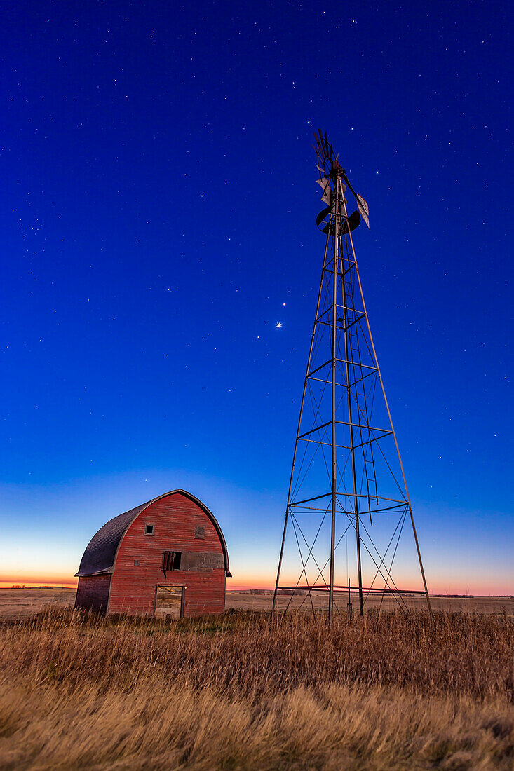 Mars, Venus and Jupiter (in that order from top to bottom) in a triangle, in conjunction, at an old farmstead near Vulcan, Alberta, in the morning twilight, October 28, 2015. Illumination is from the nearly Full Hunter’s Moon in the west. The trio of planets were in Leo in a fine conjunction not to be repeated until November 21, 2111. Almost all of Leo is visible here, with Regulus, the constellation’s brightest star, just to the right of the windmill blades at top.