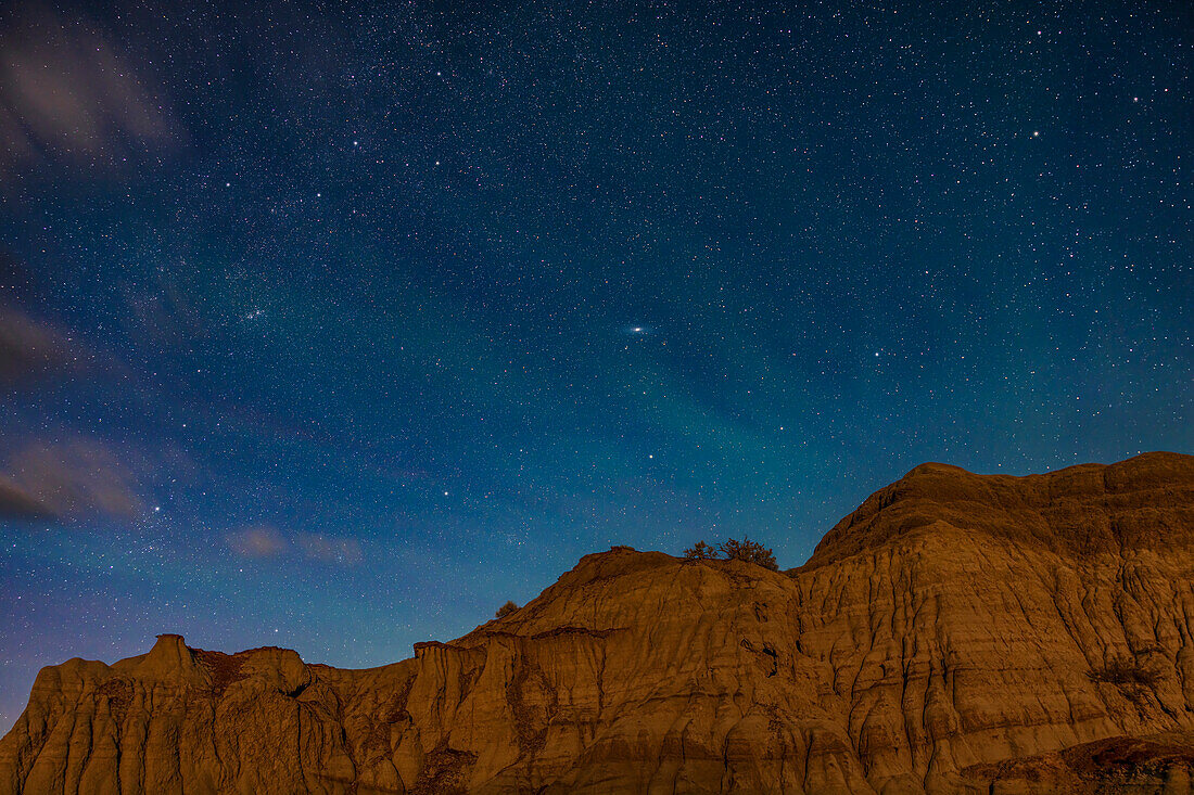 The northern autumn constellations of Pegasus (partially seen at right), Andromeda (across the centre), Perseus (at lower left) and Cassiopeia (at upper left) rising over moonlit formations at Dinosaur Provincial Park, Alberta. Illumination is from the waxing gibbous Moon, setting in the southwest so it is providing a warm "bronze-hour" light. The Andromeda Galaxy, M31, is at centre. The star clusters NGC 752, M34 and the Double Cluster are at left, as well as the Perseus OB Association of stars. Some of the small star clusters in Cassiopeia are resolved as well.