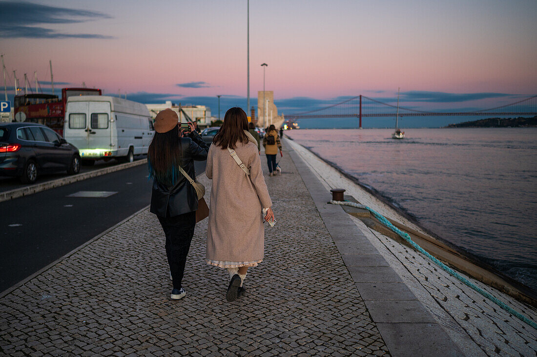 Menschen genießen den Sonnenuntergang an der Promenade von Belem am Fluss Tejo, Lissabon, Portugal