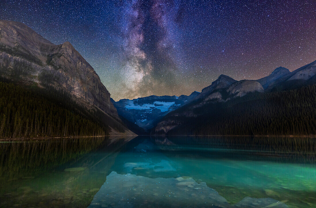 Galaxie und Gletscher! Die Milchstraße über dem von Gletschern gespeisten Lake Louise und dem Victoria Glacier im Banff National Park, Alberta. Die Scutum-Sternwolke geht gerade über dem Victoria Glacier unter, begleitet von Sternhaufen in Serpens und Ophiuchus. Der Himmel über den Bergen ist durch das Glühen der Luft grün und magenta gefärbt.