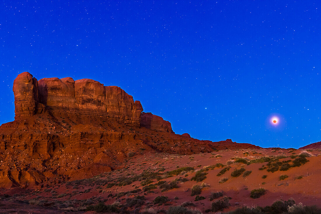 Die totale Mondfinsternis vom 4. April 2015 bei Sonnenaufgang über dem Tear Drop Arch Mesa im Monument Valley, Utah. Dies ist eine Mischung aus drei Belichtungen: eine 44-Sekunden-Aufnahme bei f/3,5 und ISO 800 für den Himmel (mit der Kamera auf dem Star Adventurer Tracker, um den Himmel für die scharfen Sterne zu verfolgen) und eine identische Belichtung mit ausgeschaltetem Tracker-Motor (für den scharfen Vordergrund), plus eine kurze 1-Sekunden-Belichtung für den verfinsterten Mond, die mit seinem überbelichteten Bild gemischt wurde. Alle Aufnahmen wurden mit dem 16-35-mm-Objektiv bei 26 mm 