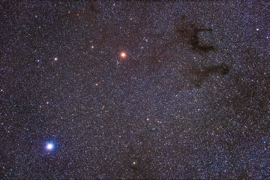 A framing of the field around the bright white star Altair (lower left), and the orange giant star Tarazed above, with the dark nebula complex B142 (lower dark lane) and B143 (the top pair of dark lanes), together known as Barnard's E. These are all in Aquila.