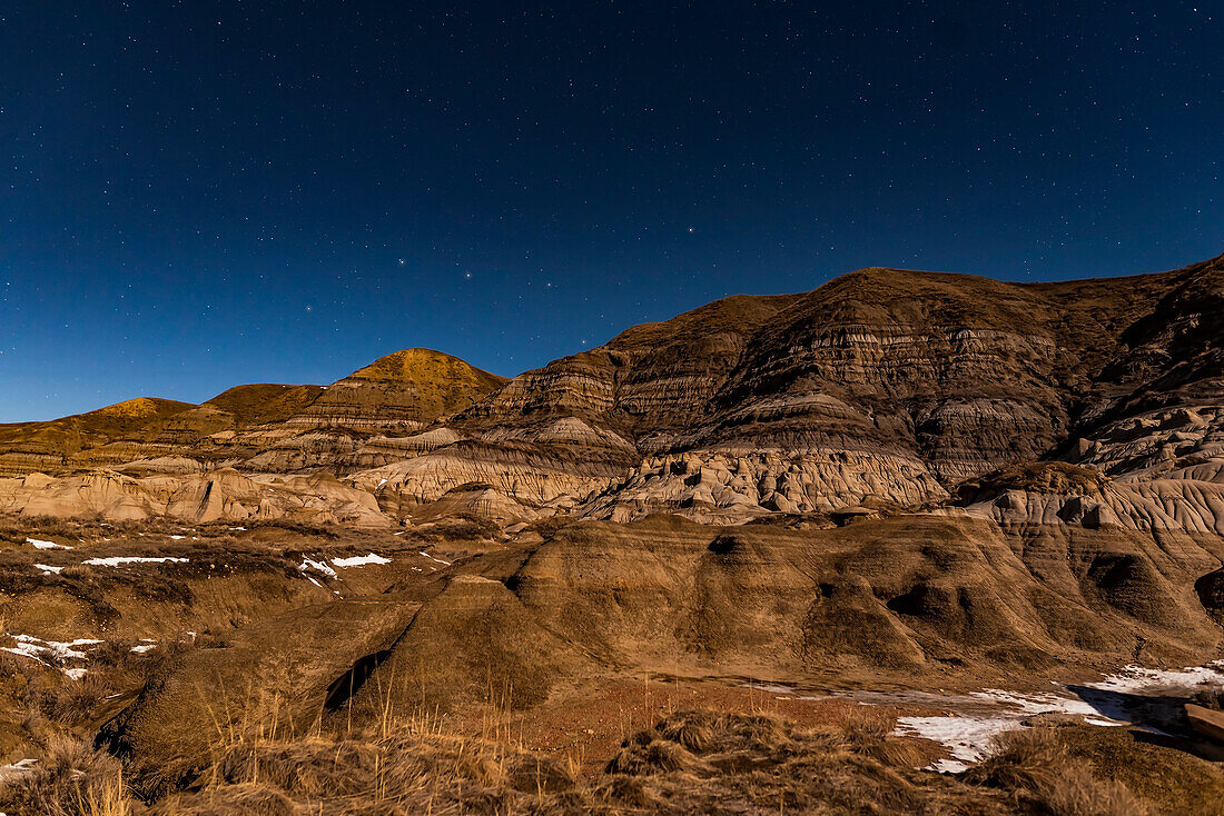 Der Große Wagen taucht an einem Spätherbst- oder Frühwinterabend bei den Hoodoos im Tal des Red Deer River in der Nähe von Drumheller, Alberta, unter die Badland-Hügel. Die Beleuchtung erfolgt durch den zunehmenden Gibbous-Mond.