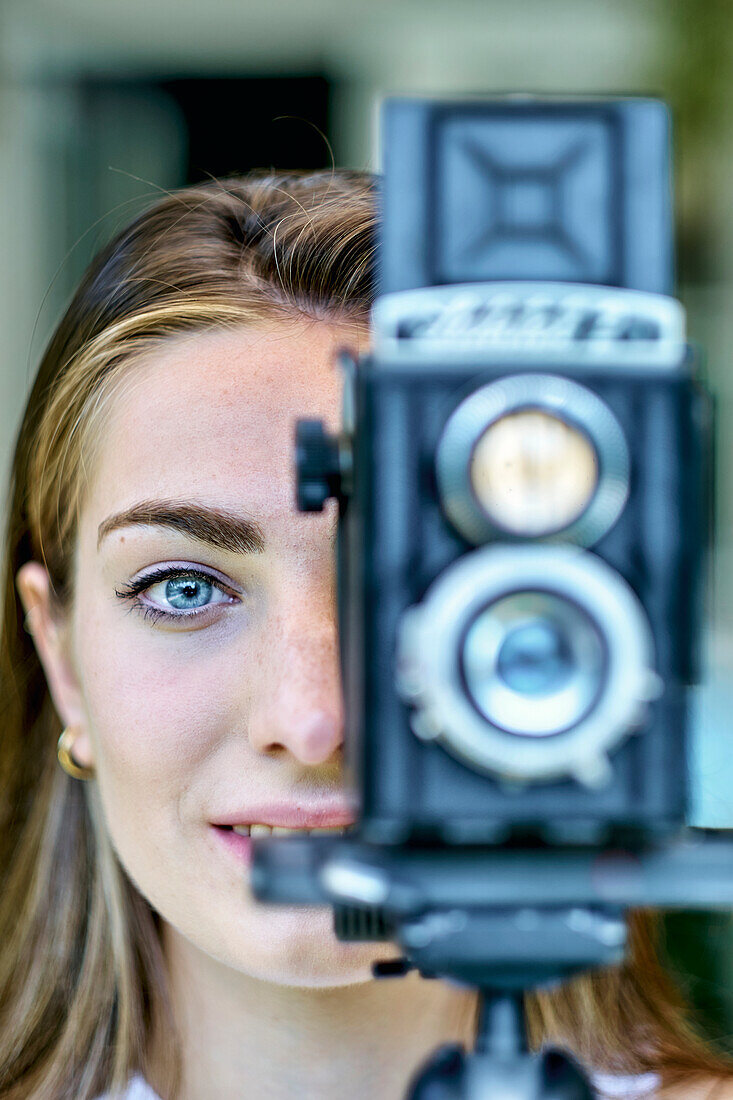 Portrait of a young beautiful caucasian woman in her 20´s with blue eyes photographing with an old vintage camera on a tripod outdoor. Lifestyle concept.