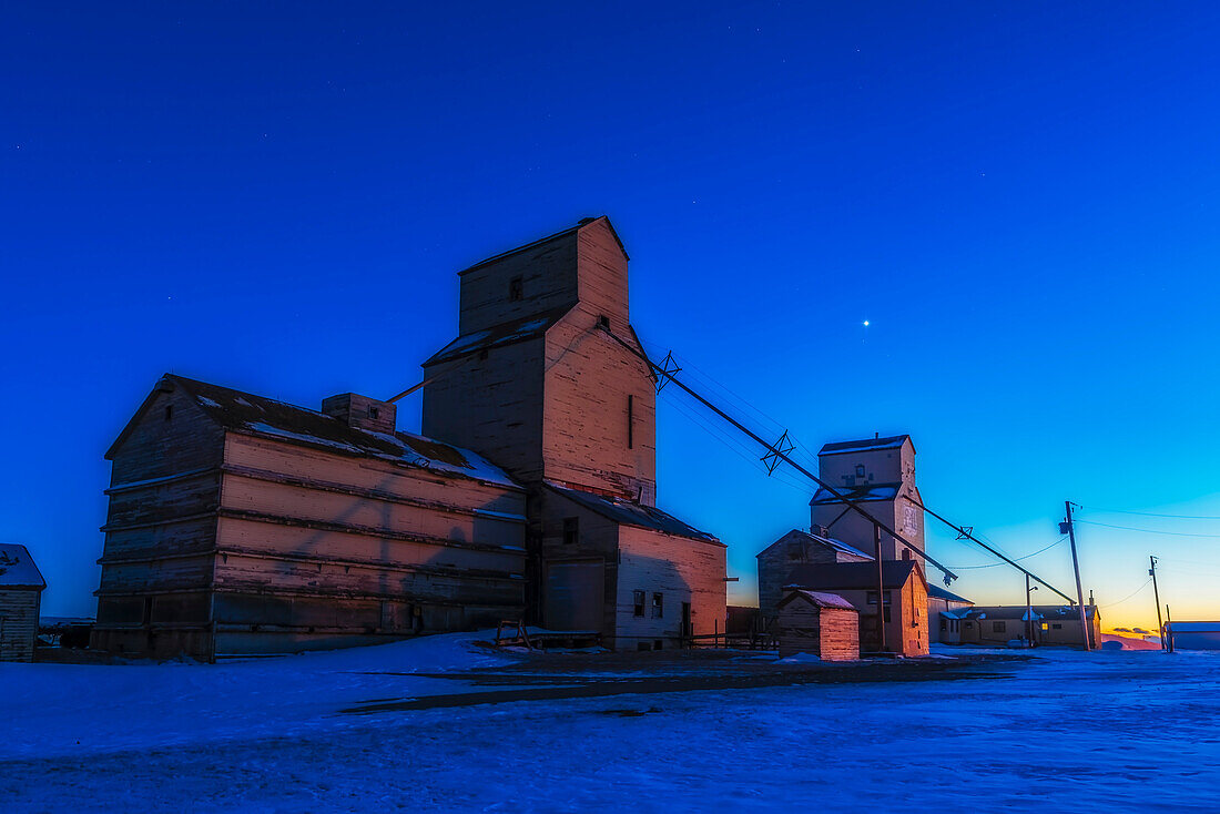 Venus, als Abendstern in der westlichen Dämmerung einer Dezembernacht, über den alten Pioneer Getreidesilos in Mossleigh, Alberta. Die Beleuchtung stammt vom Himmel und teilweise von nahe gelegenen Straßenlaternen.