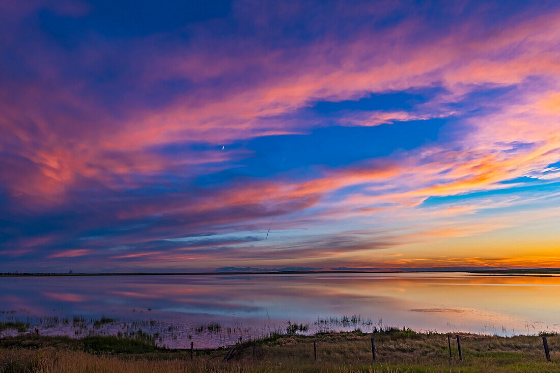 Sunset colours over Deadhorse Lake in southern Alberta, on July 8, 2016. The waxing crescent Moon shines amid the colourful clouds.