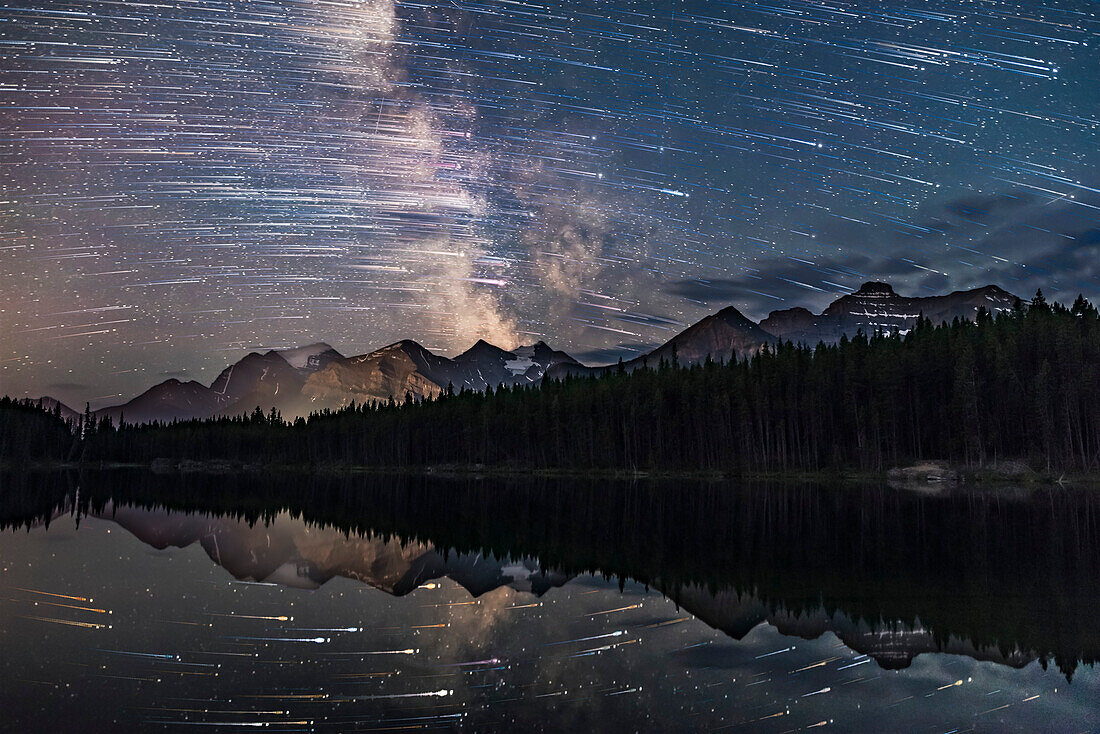 A blend of images to show the stars of the southern sky moving from east to west (left to right) over the peaks of the Continental Divide at Herbert Lake near Lake Louise, in Banff, Alberta. The main peak at left is Mount Temple.