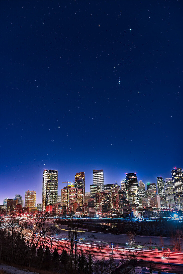 An urban nightscape of the constellations of Orion and Canis Major over the skyline of Calgary on January 18, 2018, on a very clear and moonless winter night, allowing stars to show up fairly well despite the light pollution. Sirius is above the Bow Tower building at left.