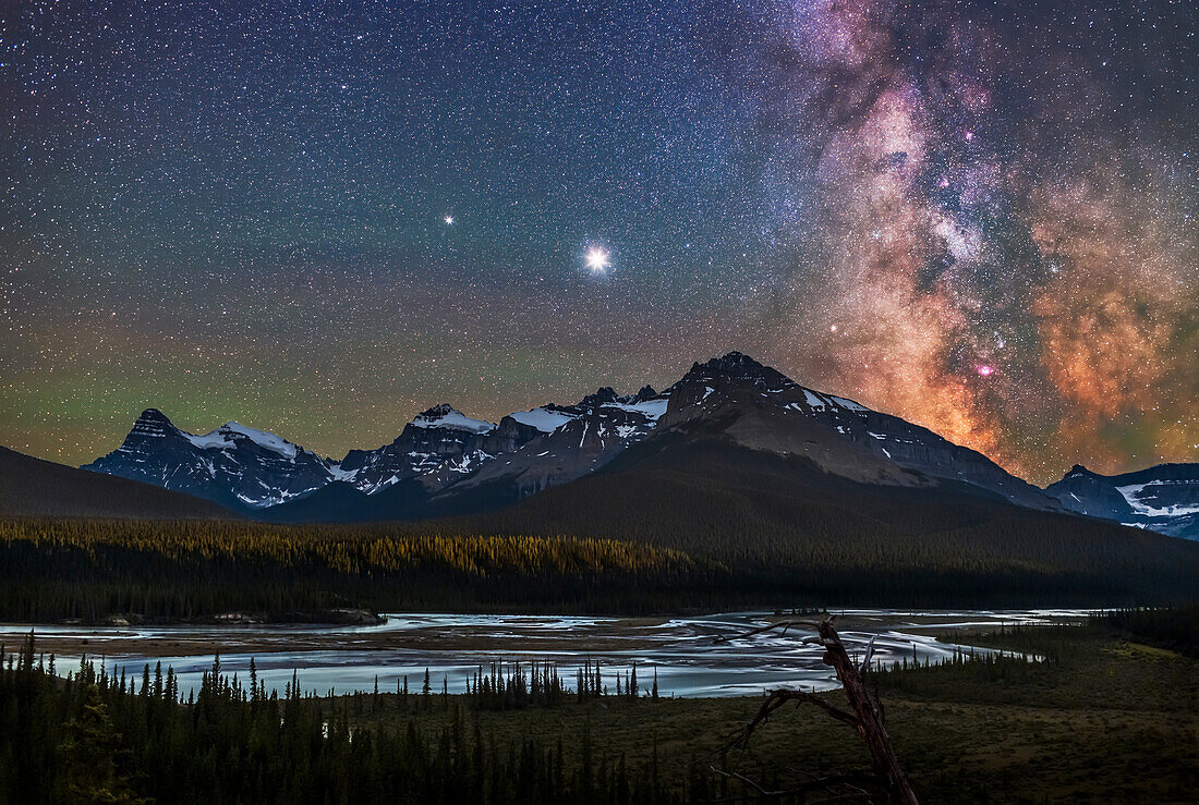 Jupiter (brightest), Saturn (to the left), and the Milky Way over the Saskatchewan River and the area of Howse Pass, on July 26, 2020. Mount Cephren is at left; the scene is framed to include Cephren. The nebulas and star clouds of the galactic centre area at right show up well on this very clear night. The bright Small Sagittarius Starcloud, aka M24, is most obvious, flanked by the star clusters M23 and M25 to the side, and the nebulas M17 and M16 above, and M8 and M20 below. The fuzzy globular cluster M22 is to the left of the large Lagoon Nebula, M8. Green airglow tints the sky.