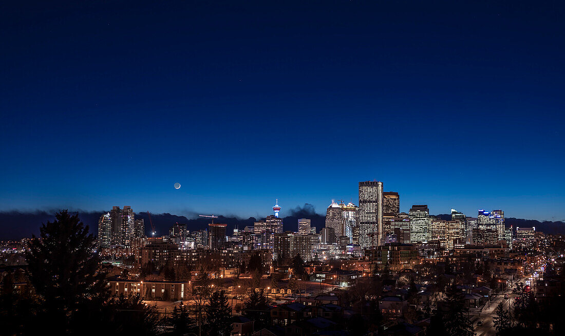 Die zunehmende Mondsichel über der Skyline von Calgary am 18. Januar 2018. Ich habe dies vom Tom Campbell Park aus aufgenommen, mit Blick nach Südwesten in die Abenddämmerung.