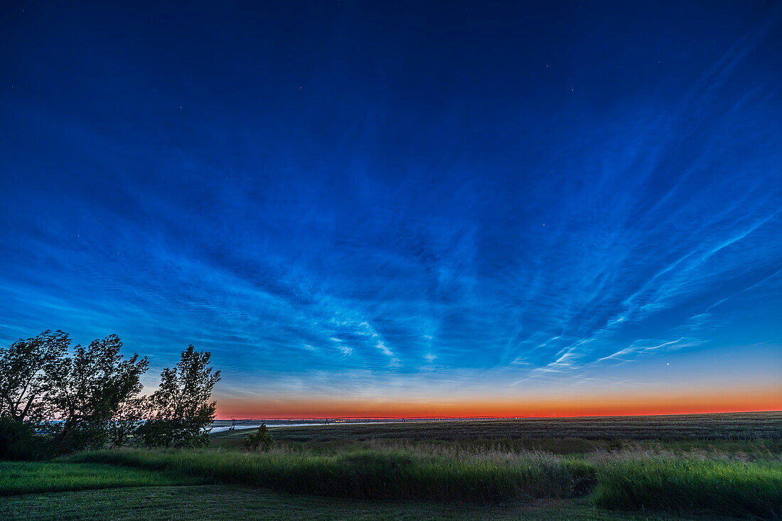 Ein großartiges und ausgedehntes Schauspiel nachtleuchtender Wolken in der Morgendämmerung des 16. Juli 2022, wobei die Wolken bis zum Zenit reichen, während sich der Himmel aufhellt. Capella ist der Stern rechts von der Mitte; die Venus geht rechts unten auf. Blick nach Nordosten in die Morgendämmerung.