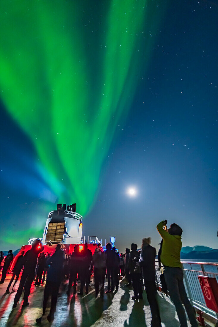 Passagiere beobachten und fotografieren die Nordlichter vom oberen Deck 9 der ms Trollfjord auf der Fahrt nach Norden, 16. Oktober 2019, nördlich von Tromsø. Die Beleuchtung erfolgt durch den abnehmenden Gibbous-Mond im Bild rechts.