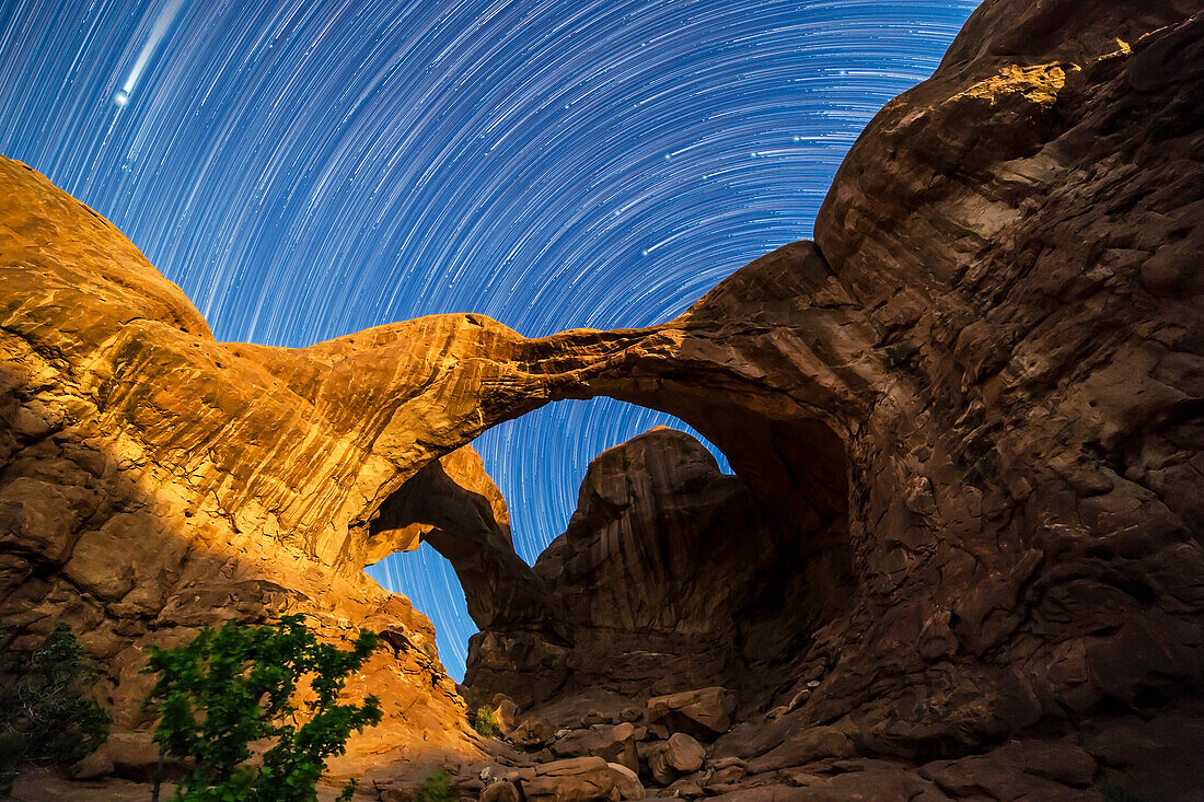 Zirkumpolare Sternspuren drehen sich hinter dem Double Arch im Arches National Park, Utah, während der abnehmende Gibbous-Mond die Bögen gegen Ende der Sequenz beleuchtet. Der Große Wagen kommt oben rechts hinter der Kuppe rechts ins Bild, während Jupiter das helle Objekt oben links ist, das in die Szene hinabzieht.