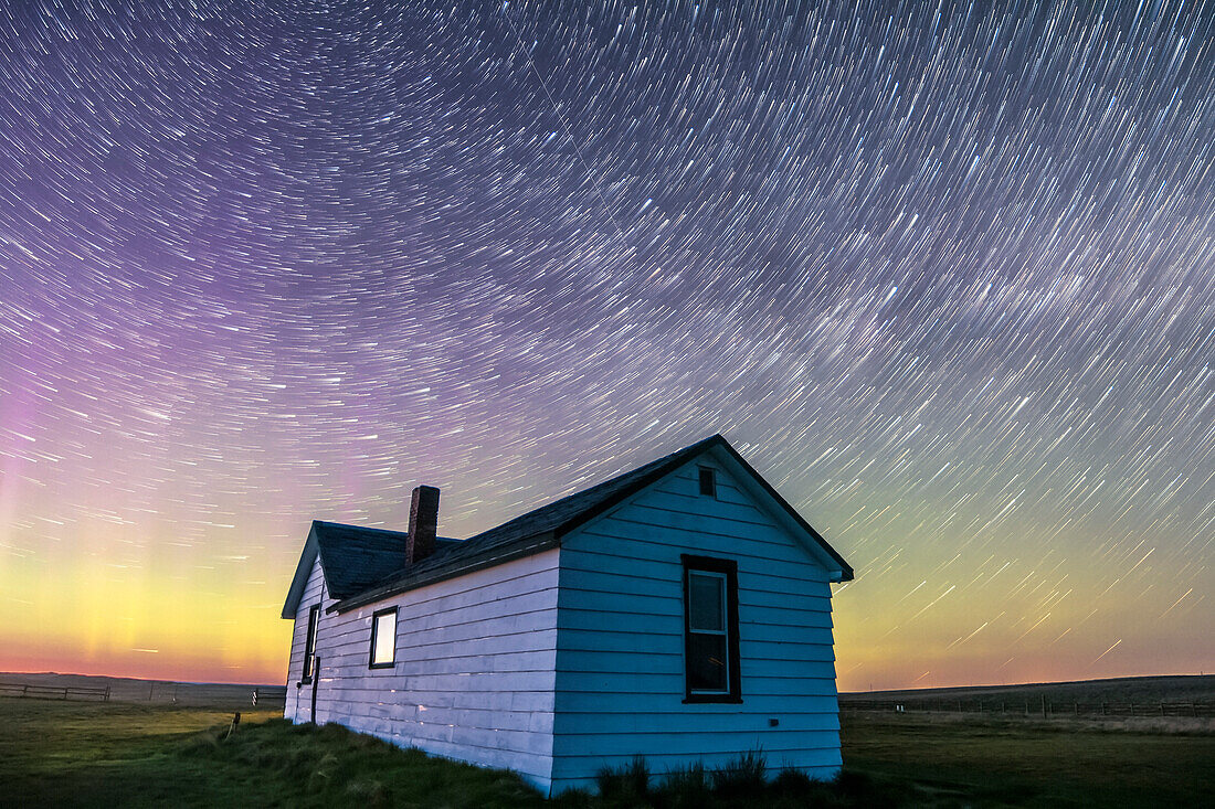 Circumpolar star trails at dawn over the historic Butala homestead at the Old Man on His Back Prairie and Heritage Conservation Area in southwest Saskatchewan, taken May 2015. This is a stack of 70 frames from a larger time-lapse sequence, from the start of the sequence in the dusk twilight, with some aurora active and adding green and magenta to the sky. Cassiopeia is at left over the house.