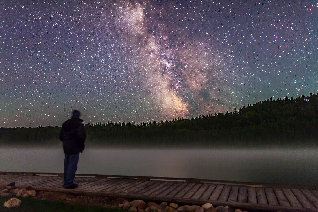 Ich posiere in der Nacht am Reesor Lake, Cypress Hills Interprovincial Park, Alberta, mit der Milchstraße über dem nebligen See. Eine einzelne 30-Sekunden-Belichtung (kein Komposit) mit dem 24-mm-Objektiv bei f/2 und der Canon 5D MkII bei ISO 3200.