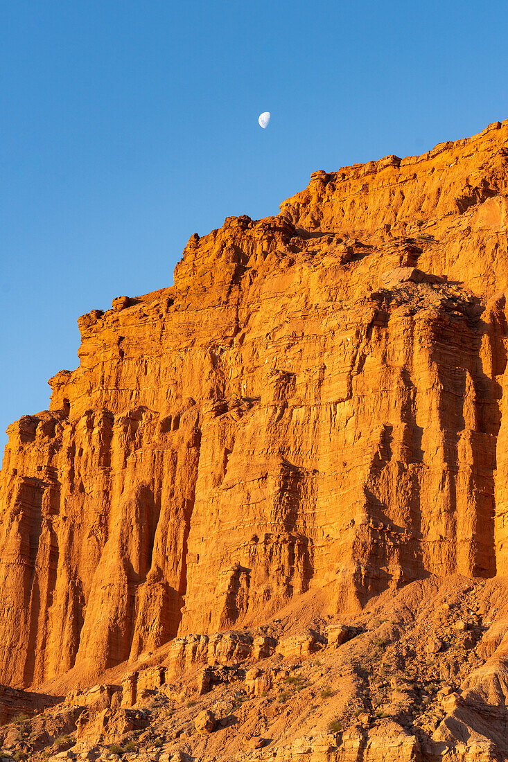 The moon over colorful red sandstone cliffs at sunset in Ischigualasto Provincial Park, San Juan Province, Argentina.