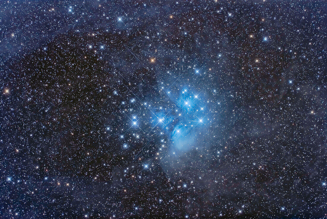 Der Sternhaufen der Plejaden, Messier 45, inmitten des schwachen und staubigen Nebels, der ihn umgibt. Die Sterne der Plejaden ziehen durch die Staubwolken im Stier und lassen sie als Beispiele für Reflexionsnebel aufleuchten.