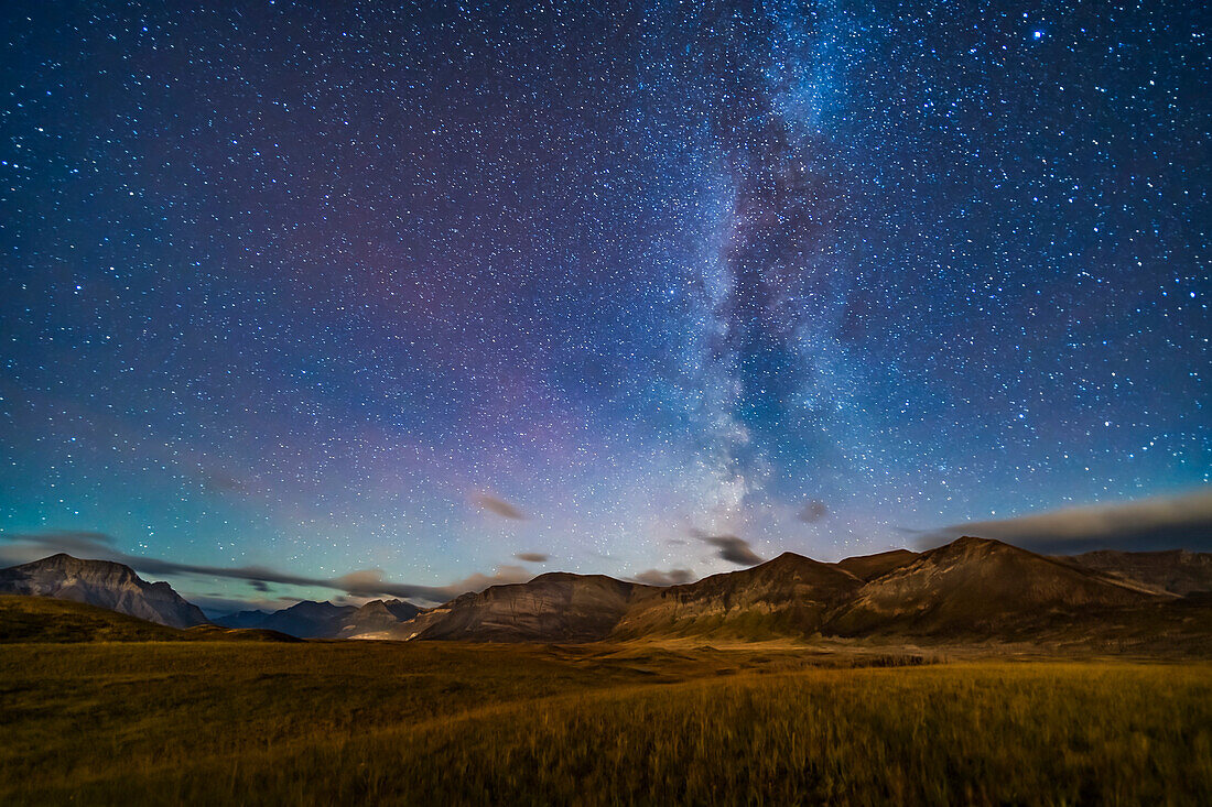 Die nördliche Sommermilchstraße, die über den Bergen des Waterton Lakes National Park, Alberta, Kanada, untergeht, mit warmem, goldenem Licht, das vom aufgehenden abnehmenden Mond (hinter der Kamera) geliefert wird und die Landschaft und den Himmel in einem Mondschein-Effekt beleuchtet. Aufgenommen am 21. September 2019 in Bildern, die als Teil eines Zeitraffers aufgenommen wurden. Der Himmel ist schwach rot gefärbt, obwohl die blaue Farbe des Himmels vom Mondlicht herrührt. Dies ist eine Aufnahme während der goldenen Stunde des Mondes.