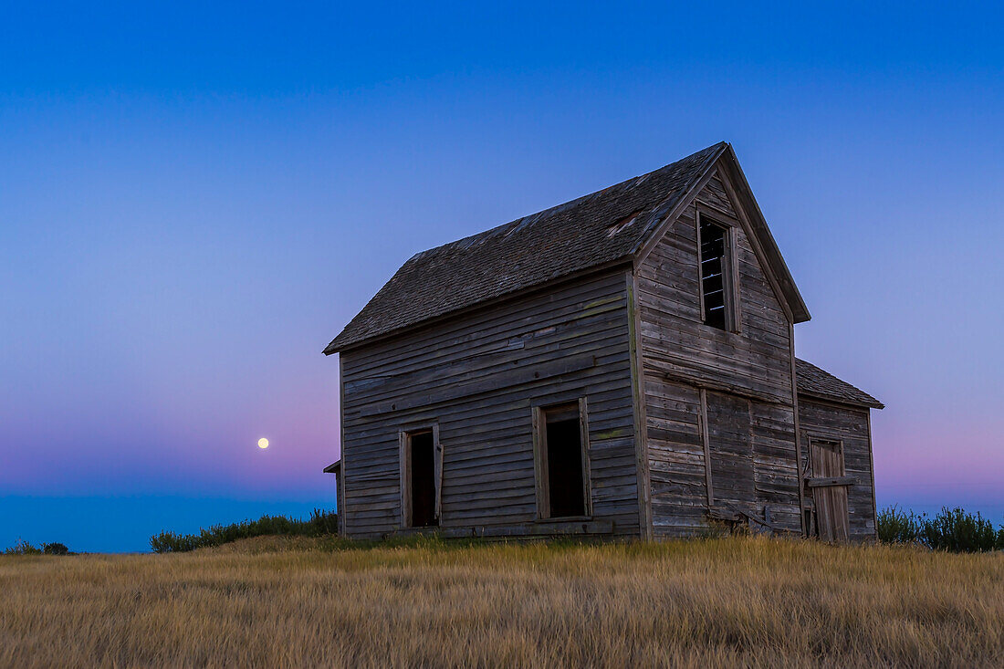 Der aufgehende fast volle Mond, ein Blaumond vom 30. Juli 2015, geht hinter einem rustikalen alten Bauernhaus in der Nähe von Bow Island, Alberta, auf. Der Mond befindet sich im Venusgürtel mit dem blauen Schatten der Erde darunter. Dies ist ein Einzelbild aus einer Zeitraffersequenz mit 600 Bildern, aufgenommen mit der Canon 6D und dem 16-35mm Objektiv.