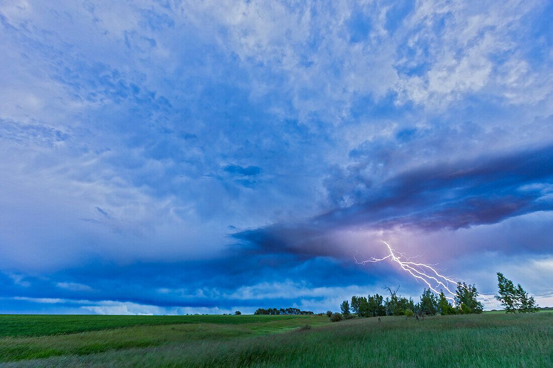 A lightning bolt comes out of a retreating thunderstorm, in the darkening twilight.