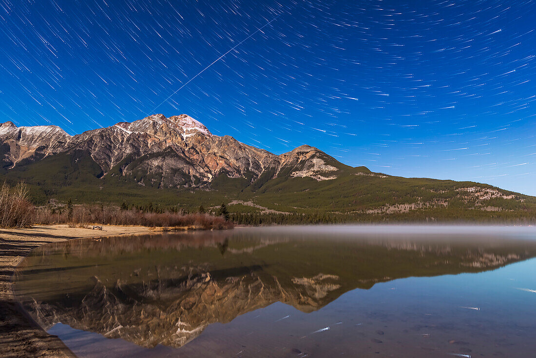 The Big Dipper (at right) trailing over Pyramid Mountain in Jasper National Park, on a moonlit night on October 24/25, 2015. An Iridium satellite, in fact two following each other on the same path, streak at left.