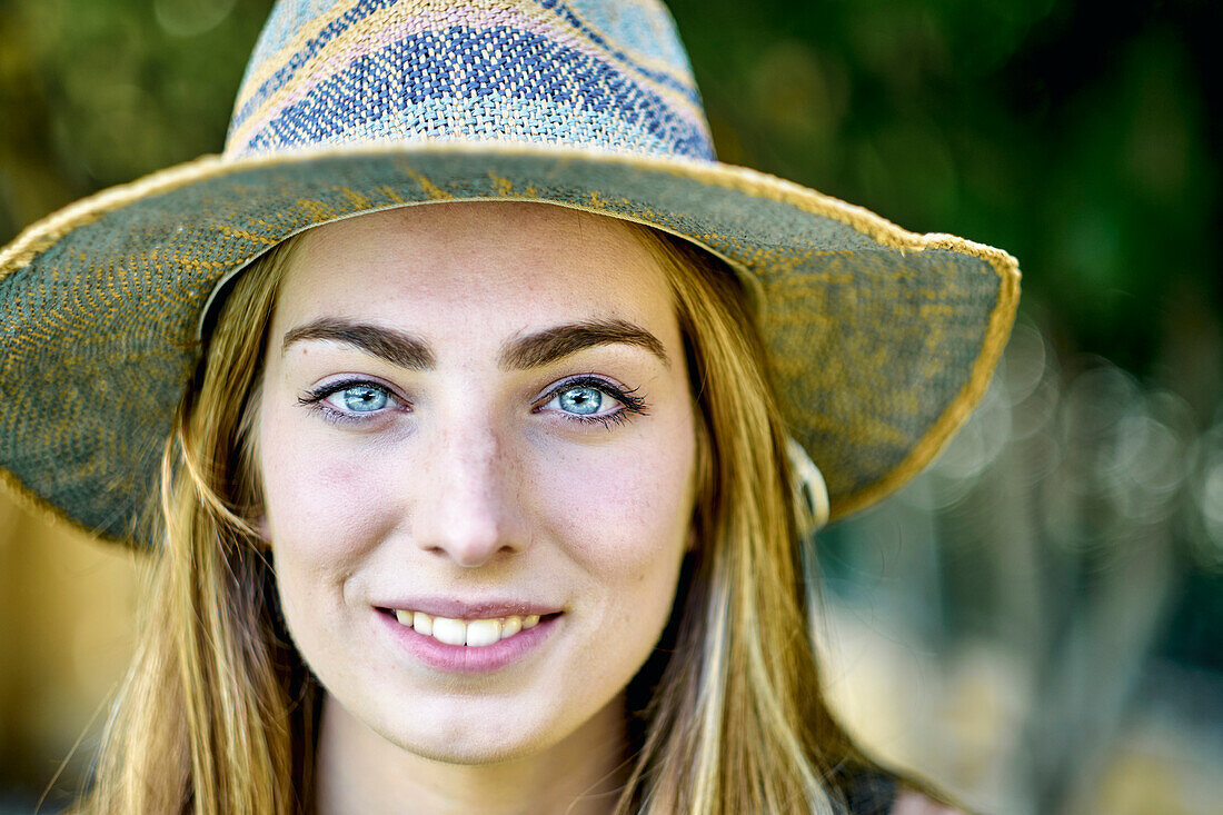 Natürliche Schönheit Porträt einer jungen Frau in den 20er Jahren mit langen Haaren und blauen Augen, die einen Hut im Freien in einem Garten trägt. Lebensstil-Konzept.