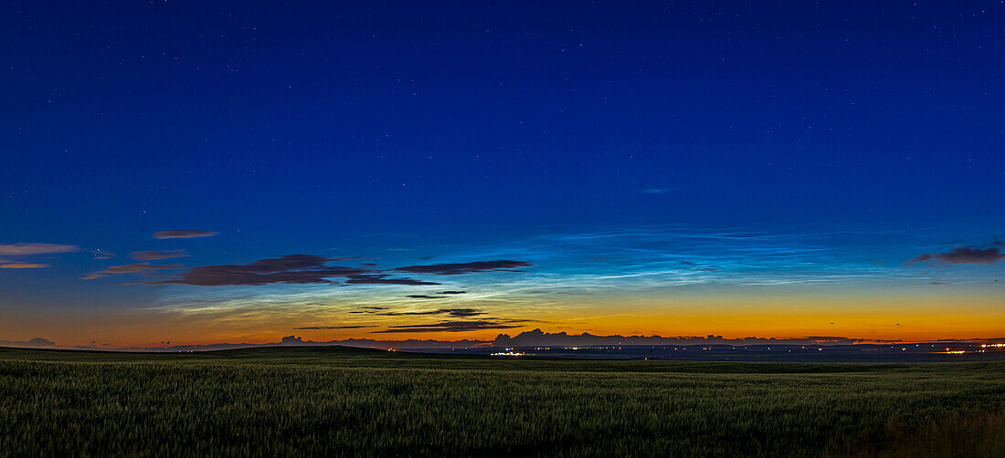 A panorama of a fairly bright display of noctilucent clouds to the northwest early in the evening on July 7, 2022. Even so, this was about 11:50 pm MDT. The bright NLCs contrast with the dark silhouettes of the closer and lower tropospheric clouds. A gibbous Moon lights the foreground.
