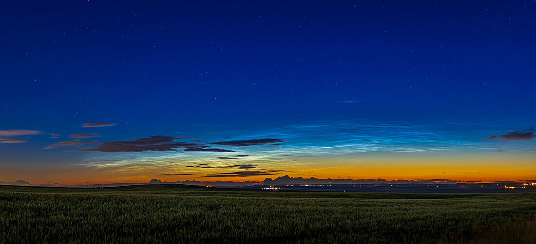 Ein Panorama eines ziemlich hellen Schauspiels nachtleuchtender Wolken im Nordwesten am frühen Abend des 7. Juli 2022. Das war allerdings gegen 23:50 Uhr MDT. Die hellen NLCs stehen im Kontrast zu den dunklen Silhouetten der näheren und unteren troposphärischen Wolken. Ein gibbouser Mond beleuchtet den Vordergrund.