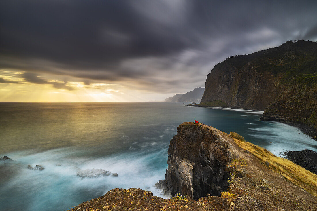 Ein Mädchen betrachtet das Meer bei Sonnenaufgang von den Klippen von Guindaste, Faial, Gemeinde Santana, Madeira, Portugal, Atlantik, Europa