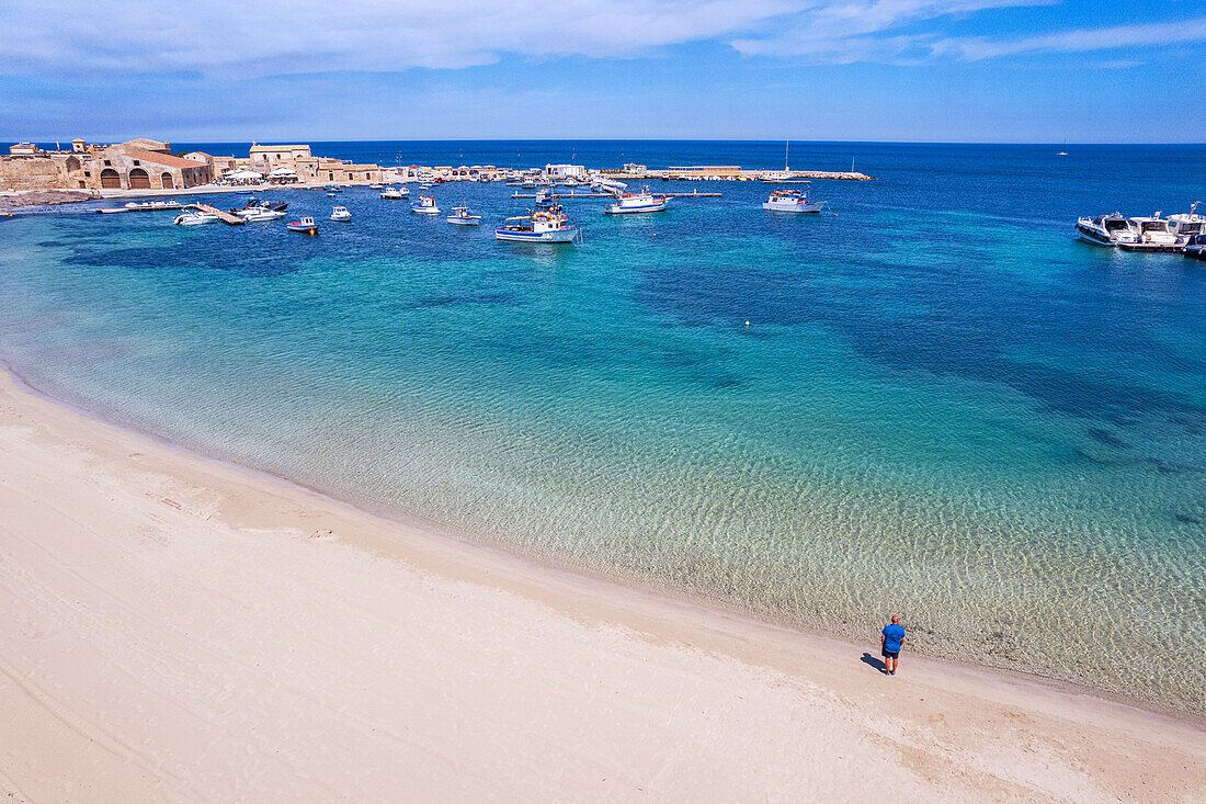 Aerial view of tourist standing in an empty white sand beach looking at the sea in front of the fishing village of Marzamemi, Marzamemi, Pachino municipality, Siracusa province, Sicily, Italy, Mediterranean, Europe