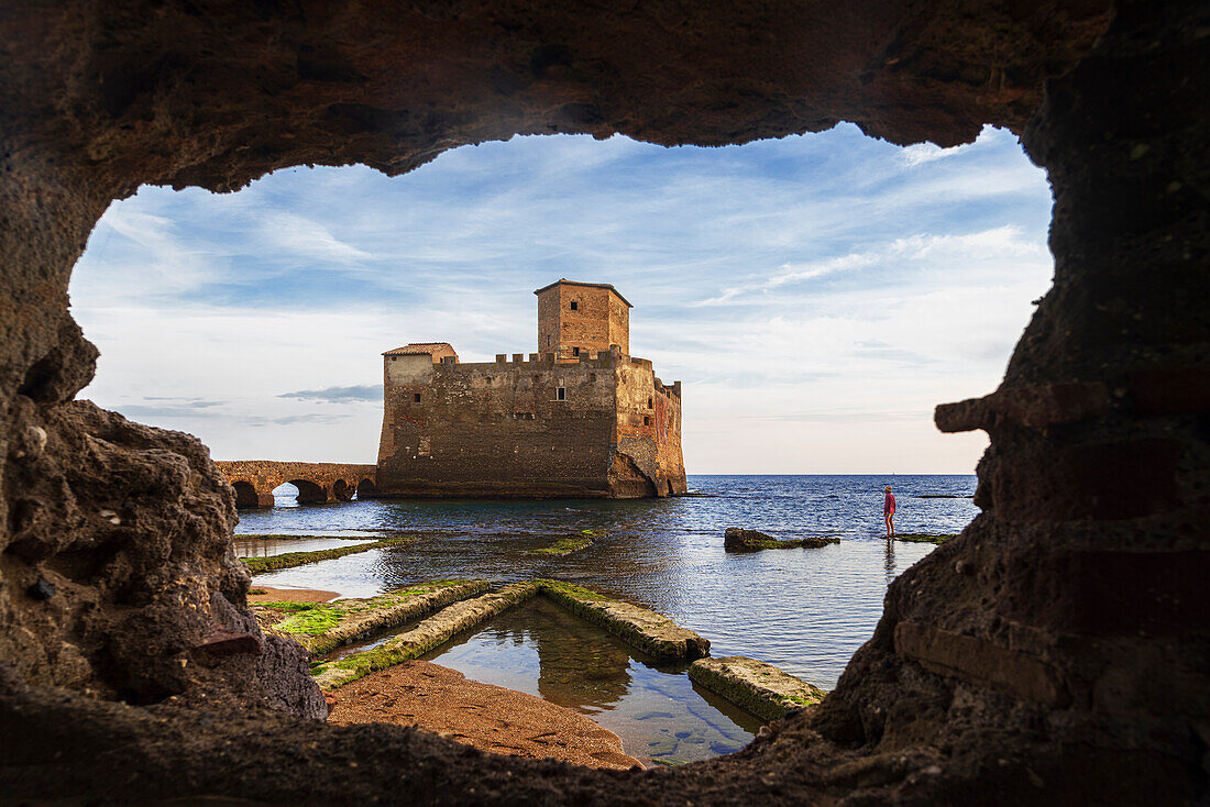 Tourist admiring the castle of Torre Astura seen through a cave in the ground, Rome province, Tyrrhenian sea, Latium (Lazio), Italy, Europe