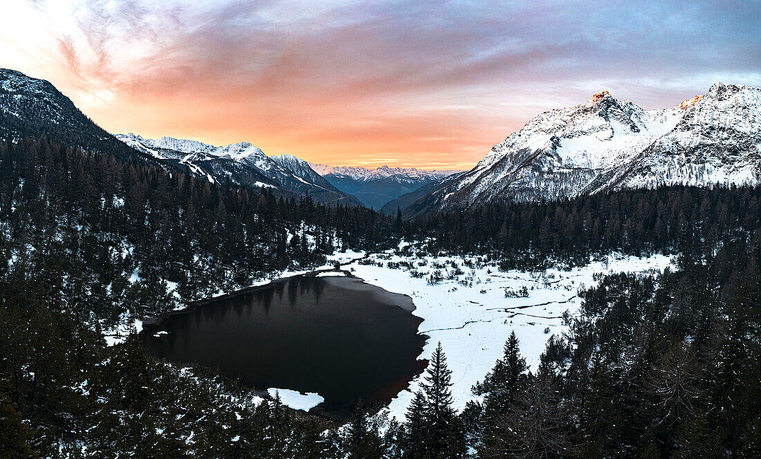 Panoramablick aus der Luft auf verschneite Wälder und den zugefrorenen Entova-See bei Sonnenaufgang, Valmalenco, Valtellina, Lombardei, Italien, Europa