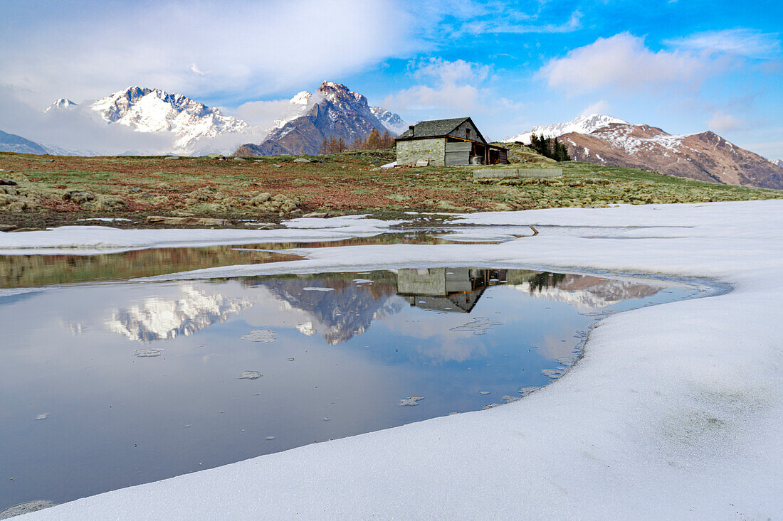 Mountain hut on shore of frozen pond during thaw, Scermendone Alp, Rhaetian Alps, Valtellina, Lombardy, Italy, Europe