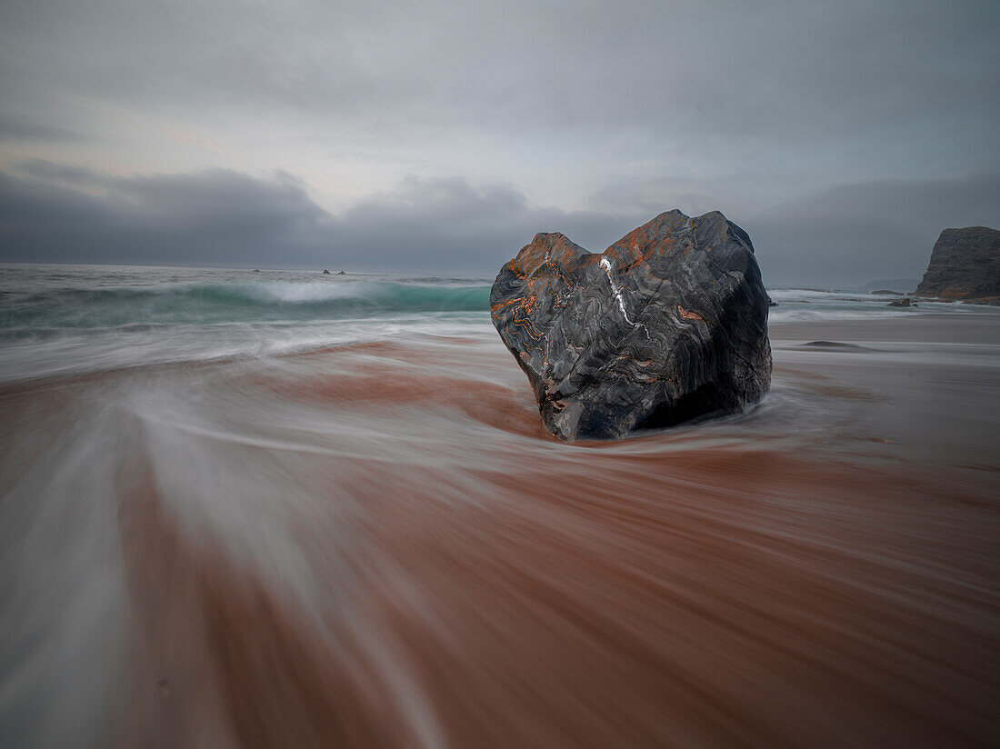Long exposure of the flowing sea and a heart shaped rock on the Portizuelo beach, Asturias, Spain, Europe