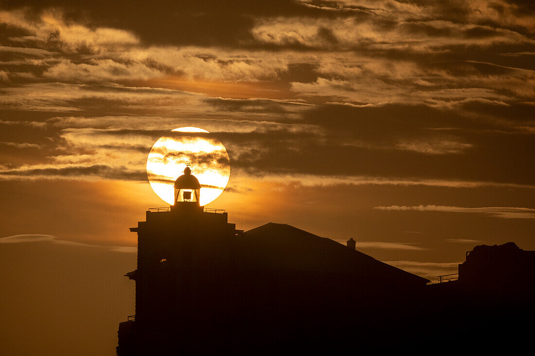 Sun aligned with the silhouette of the lighthouse of Luarca, Asturias, Spain, Europe