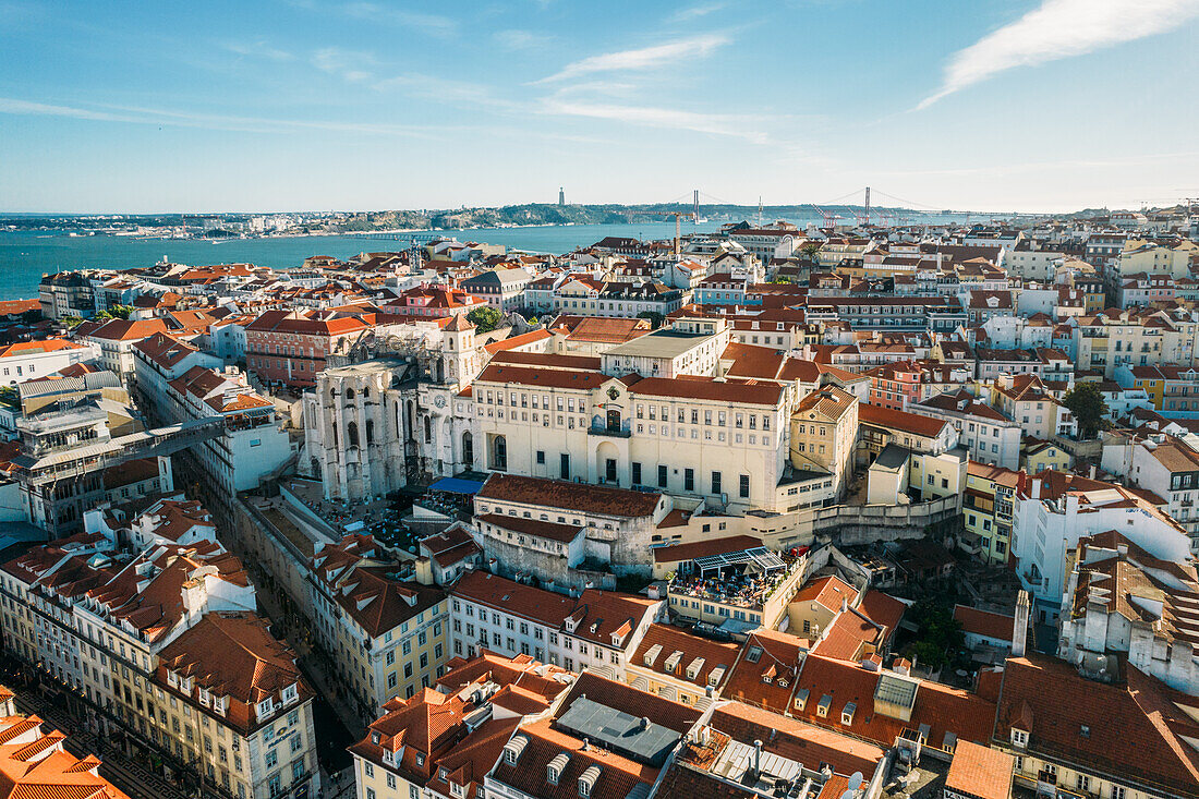 Aerial drone view of Carmo Church and surrounding historic neighbourhood in Chiado, with Tagus River and 25 April Bridge visible, Lisbon, Portugal, Europe