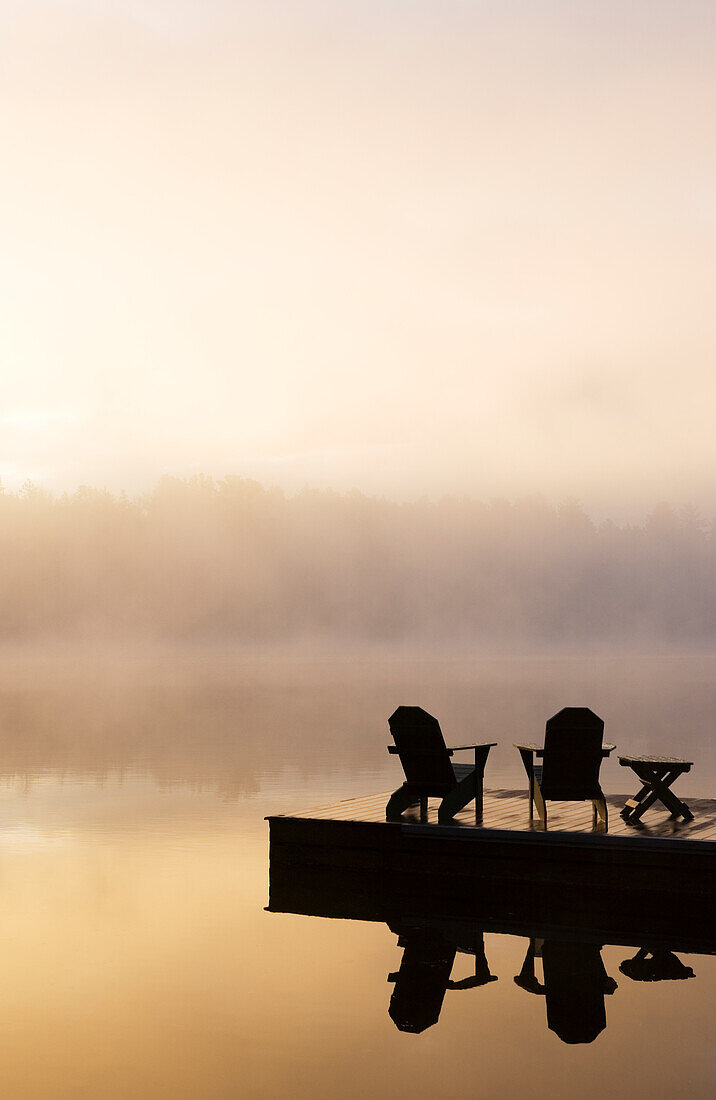 USA, New York, Silhouetten von Adirondack-Stühlen auf dem Pier am Lake Placid bei Sonnenaufgang im Adirondack Park