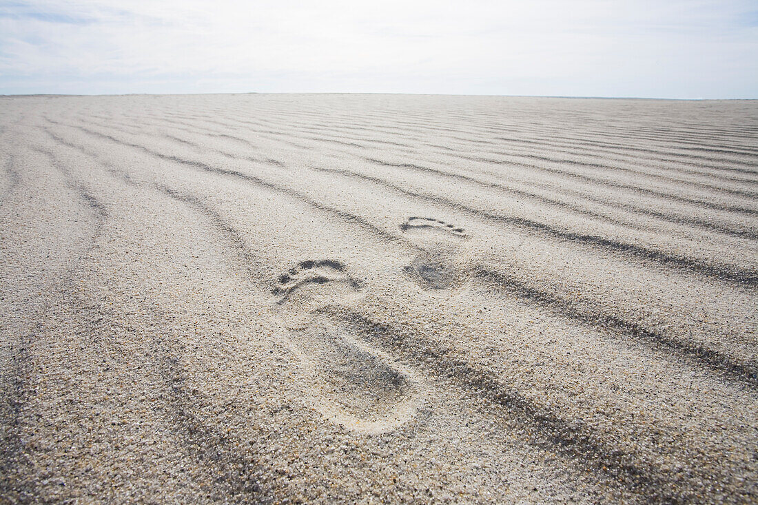 Fußabdrücke auf gewelltem Sand am Strand