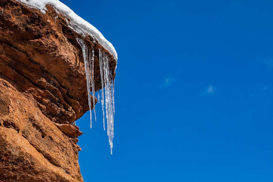 Eiszapfen hängen an Felsen vor blauem Himmel