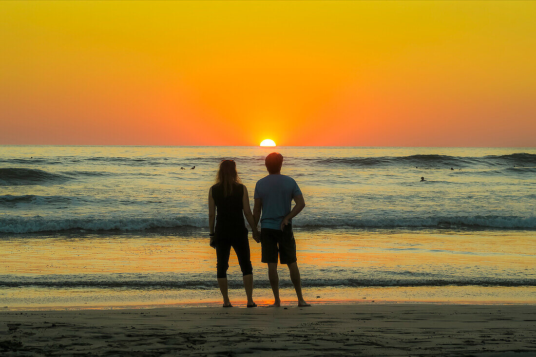 Paar hält sich am Strand von Guiones an den Händen, wo sich die Leute zum Surfen versammeln und den Sonnenuntergang beobachten, Playa Guiones, Nosara, Guanacaste, Costa Rica, Mittelamerika